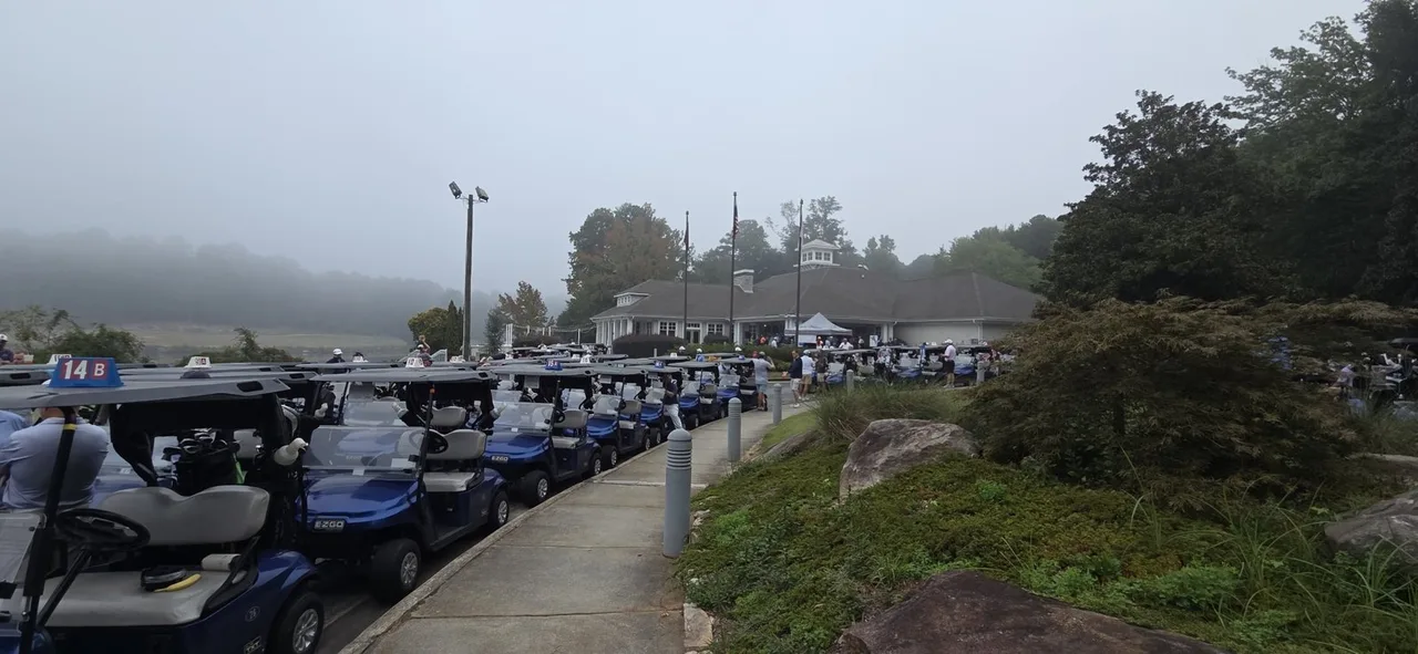 A long line of golf carts outside a clubhouse on a foggy morning, with golfers gathering before the start.